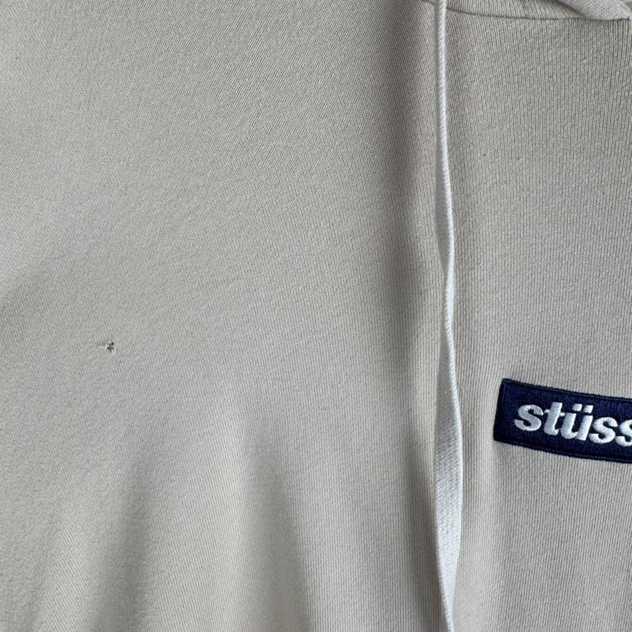 Stüssy beige oversized hoodie with embroidered box logo and small hole detail.