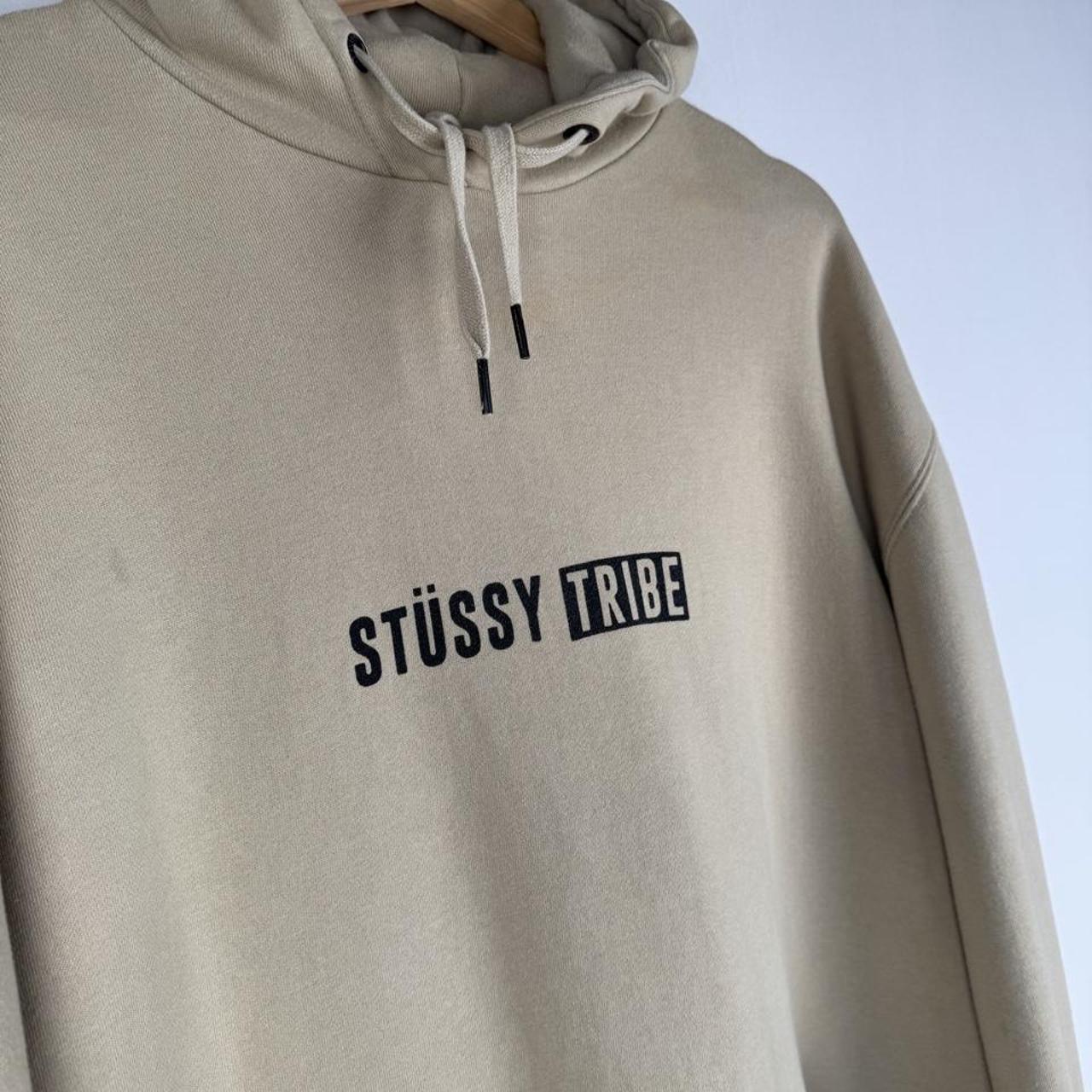 Stüssy oversized beige hoodie with Tribe spellout logo and relaxed fit.