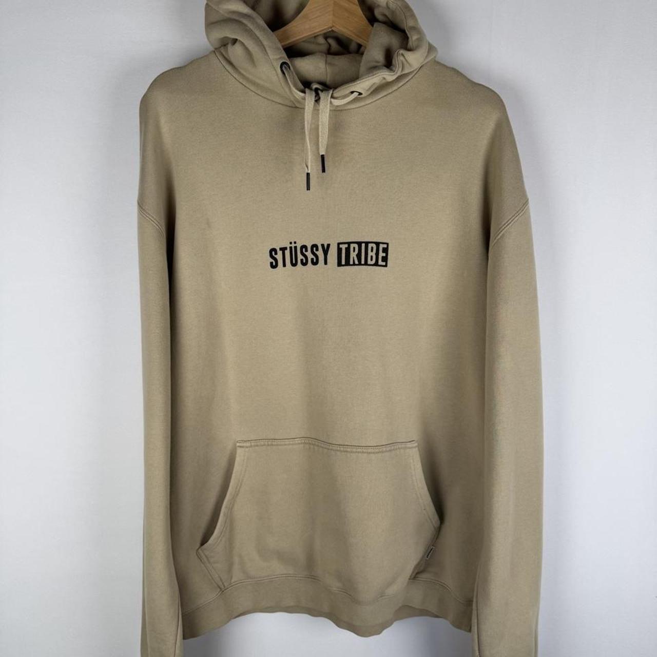 Stüssy oversized beige hoodie with Tribe spellout logo and relaxed fit.