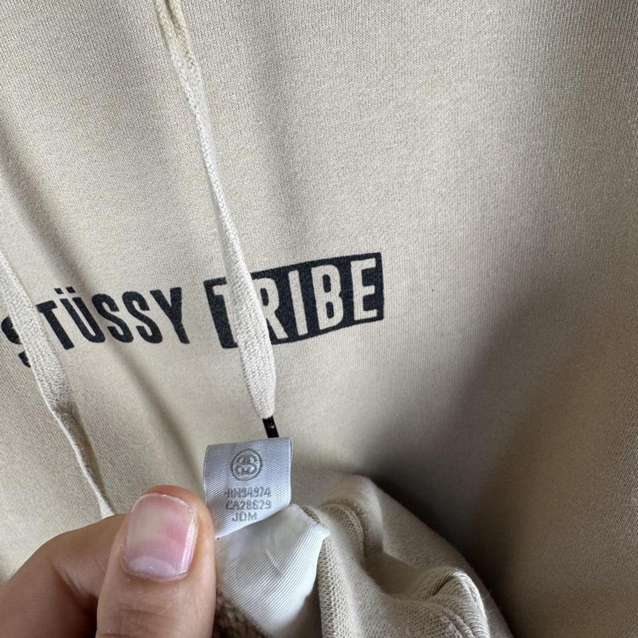 Stüssy oversized beige hoodie with Tribe spellout logo and relaxed fit.
