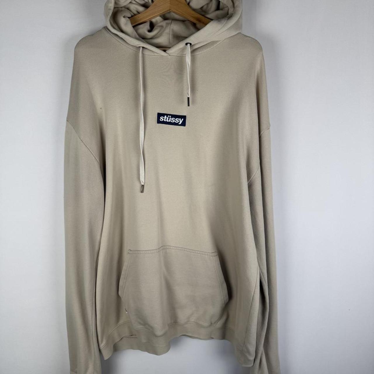 Stüssy beige oversized hoodie with embroidered box logo and small hole detail.