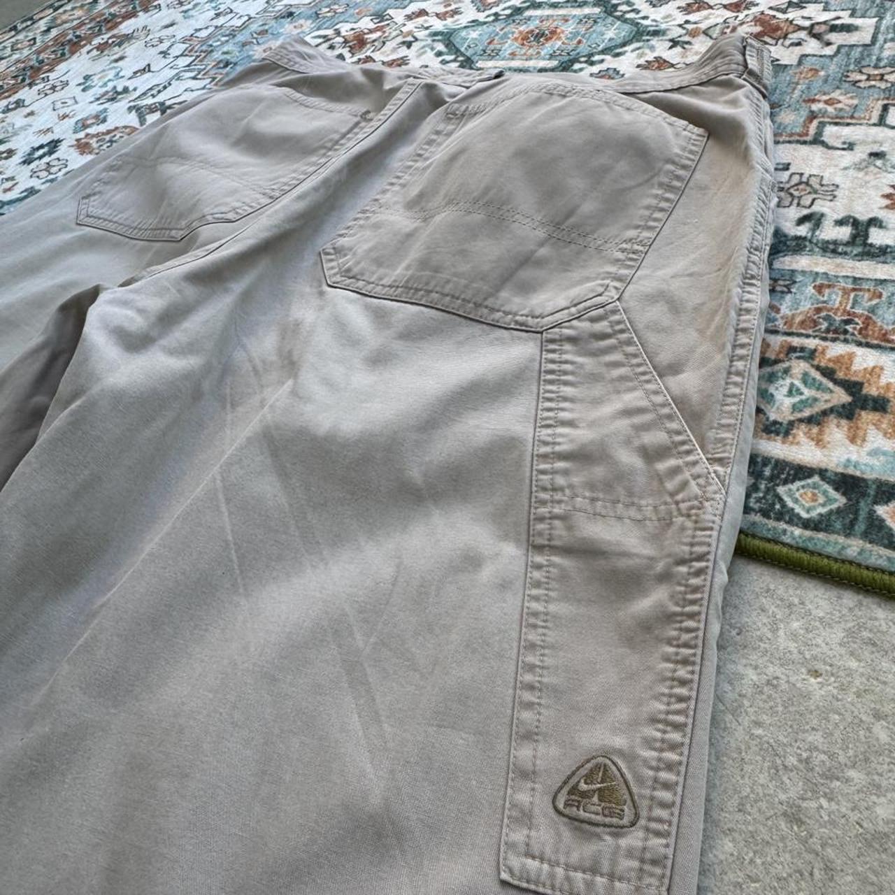 Nike ACG beige cargo pants with embroidered logo and multiple pockets.