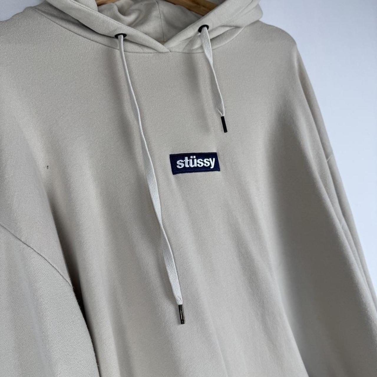 Stüssy beige oversized hoodie with embroidered box logo and small hole detail.