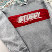 Stüssy grey sweatshirt featuring international logo and soft cotton material.