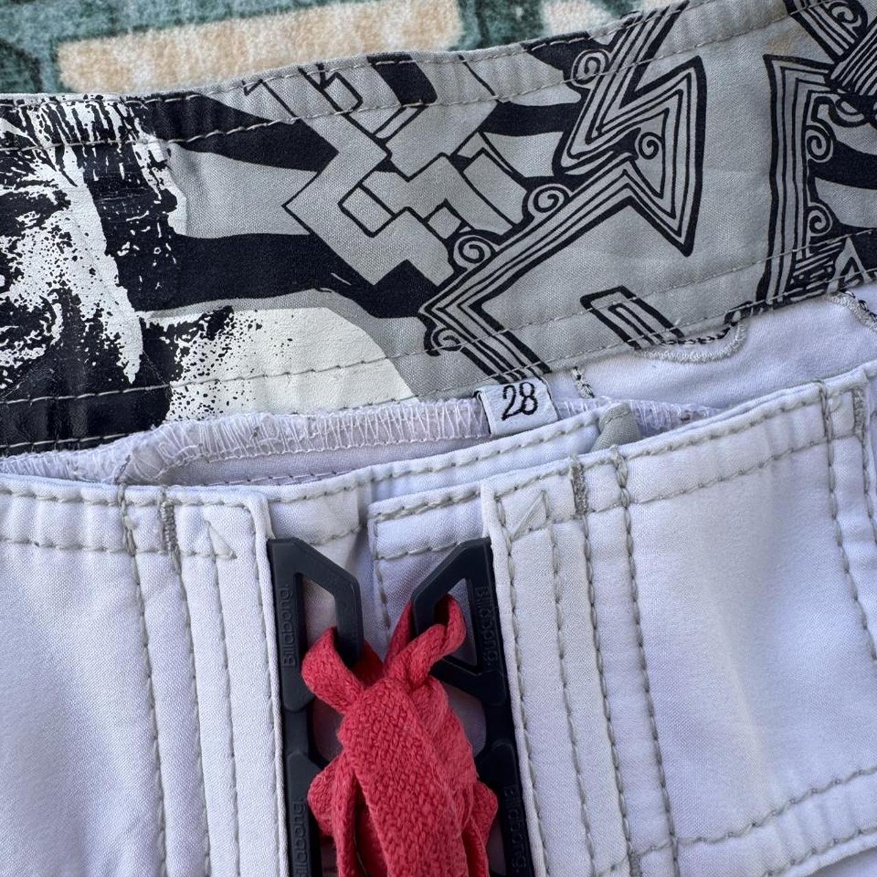 Billabong board shorts blue with embroidered Taj Burrow signature and tropical pattern.