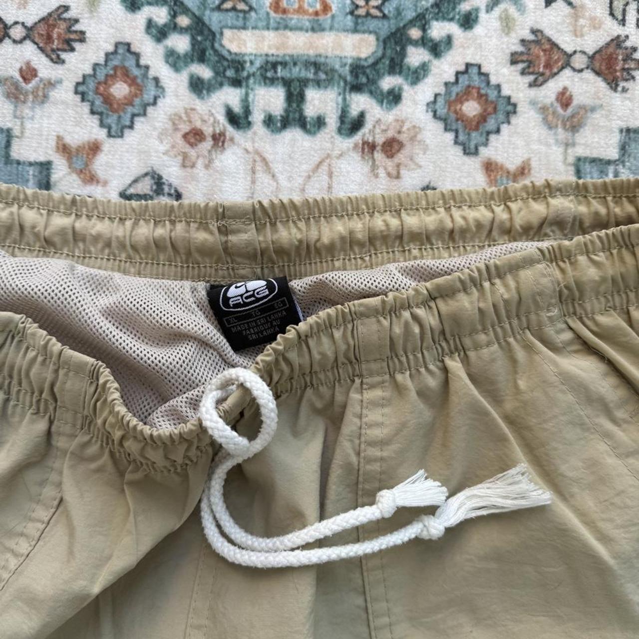 Nike ACG cream swim shorts with logo detail and lightweight material.